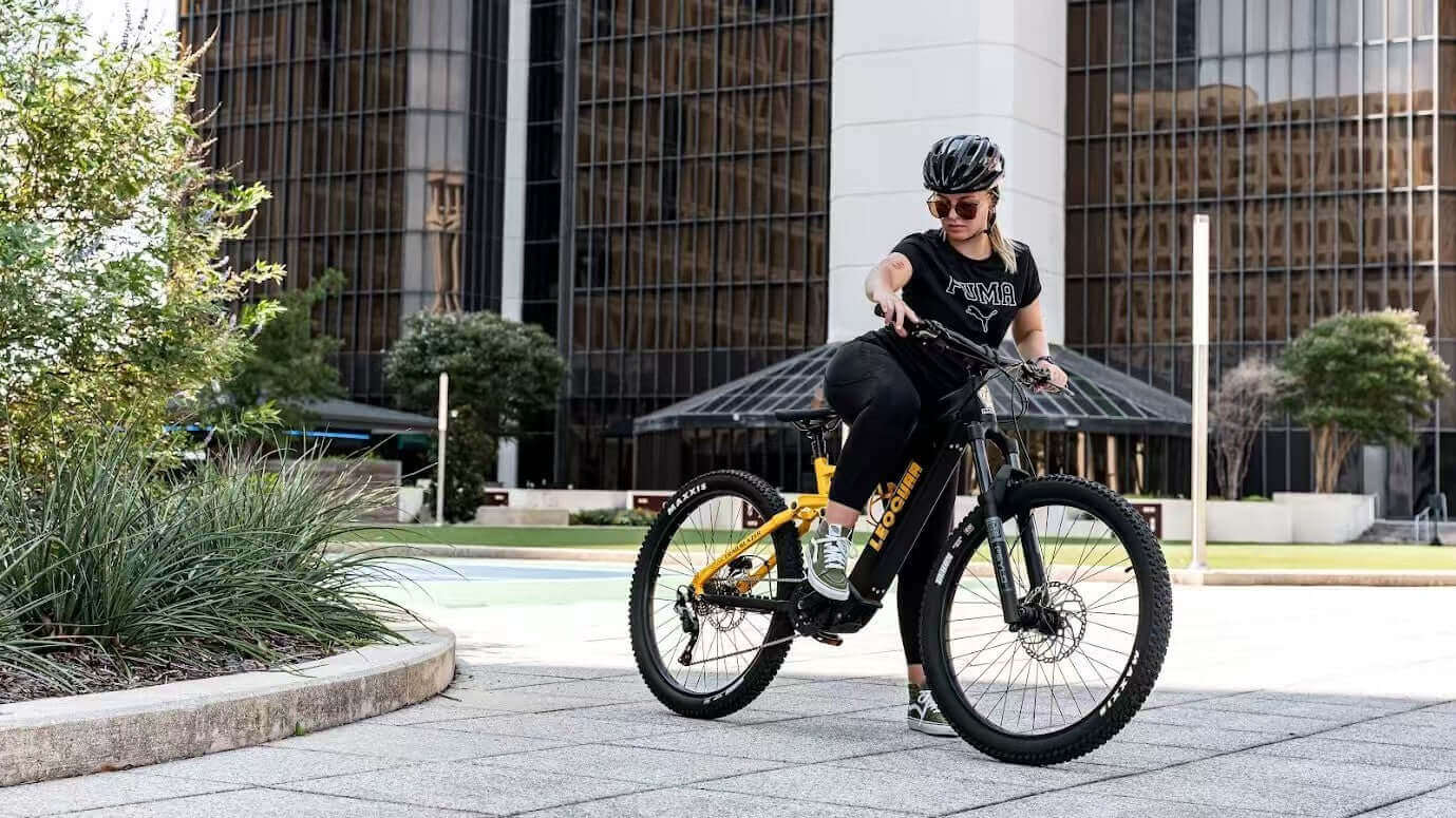 A rider on a black and yellow electric bike in an urban setting, demonstrating e-bike range and performance.
