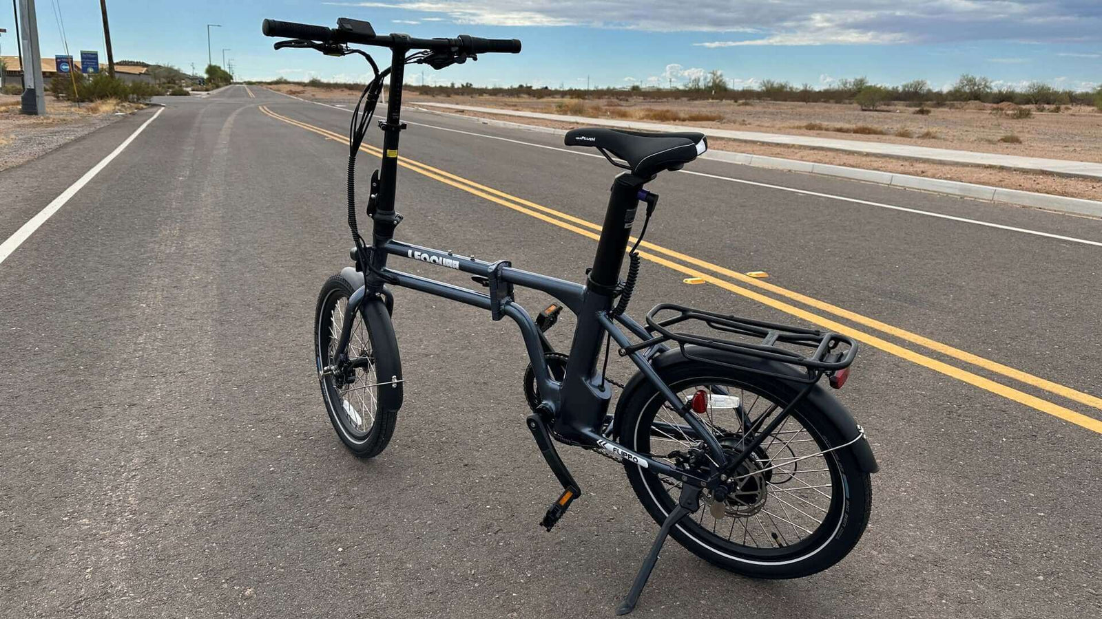 Foldable electric bike parked on a quiet highway under clear skies, showcasing compact design and portability.