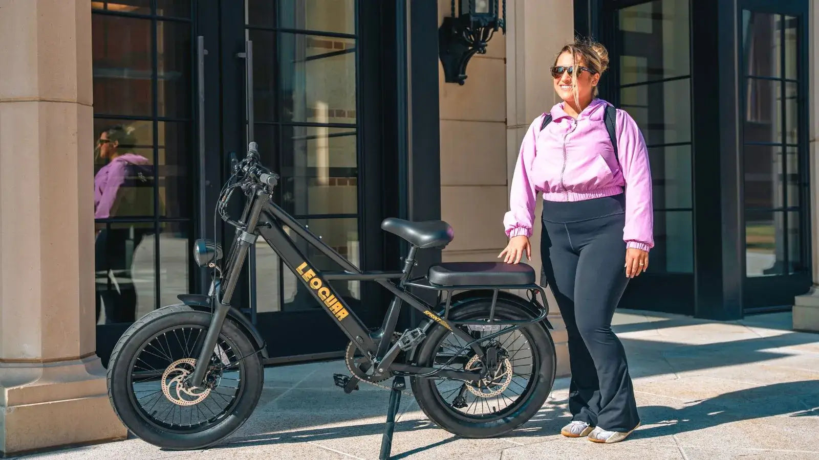 Woman standing next to a black electric bike with seat in an urban setting