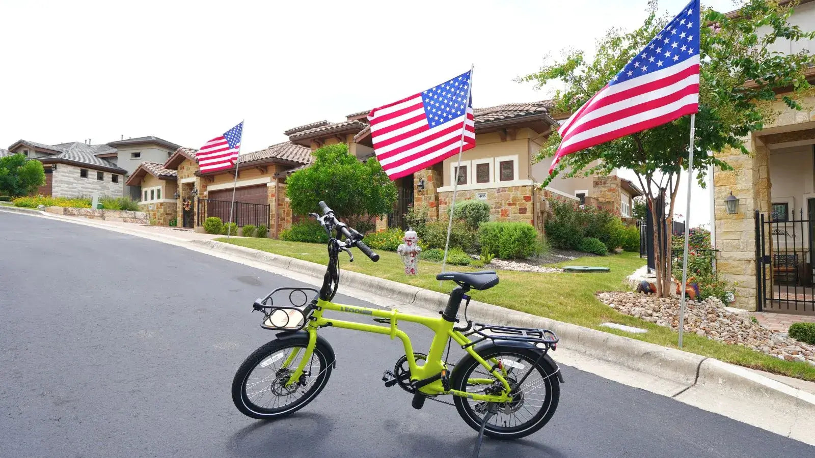 Green folding electric bike on a suburban street lined with houses decorated with American flags.