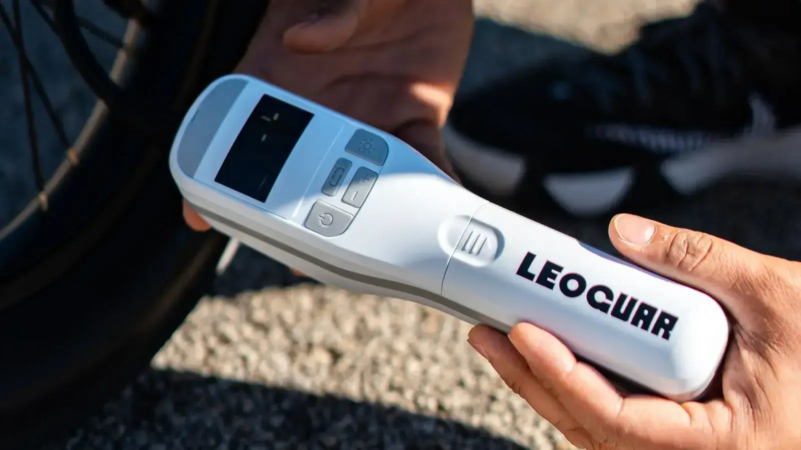 Close-up of a cyclist holding a LEOGUAR wireless tire pump near a bike wheel.