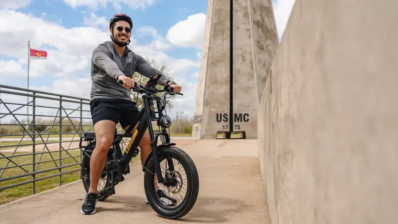 Man riding an electric fat tire bike near a monument on a sunny day, demonstrating real-world e-bike range conditions
