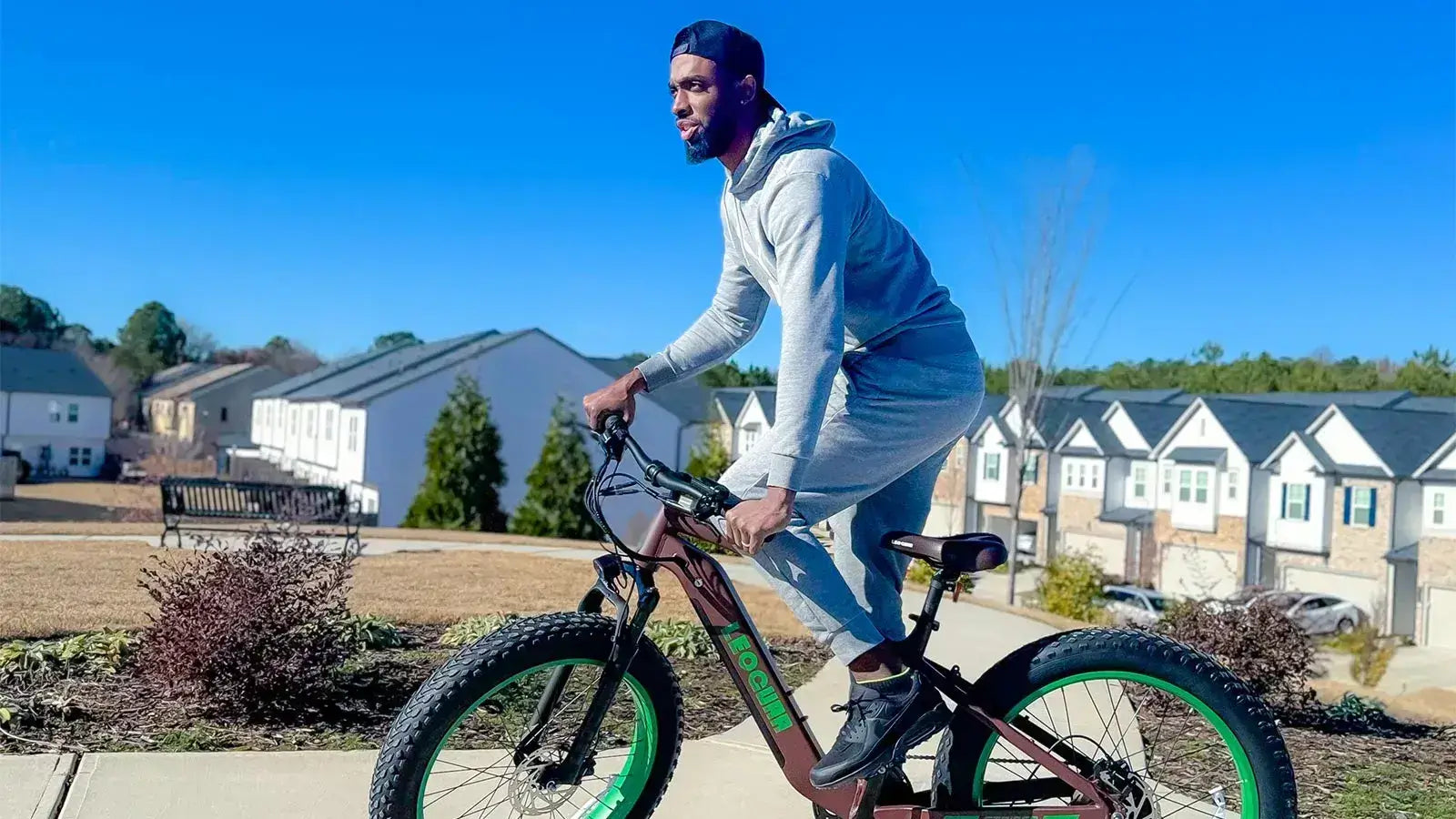 Man riding a green fat tire road e-bike through a suburban neighborhood on a sunny day