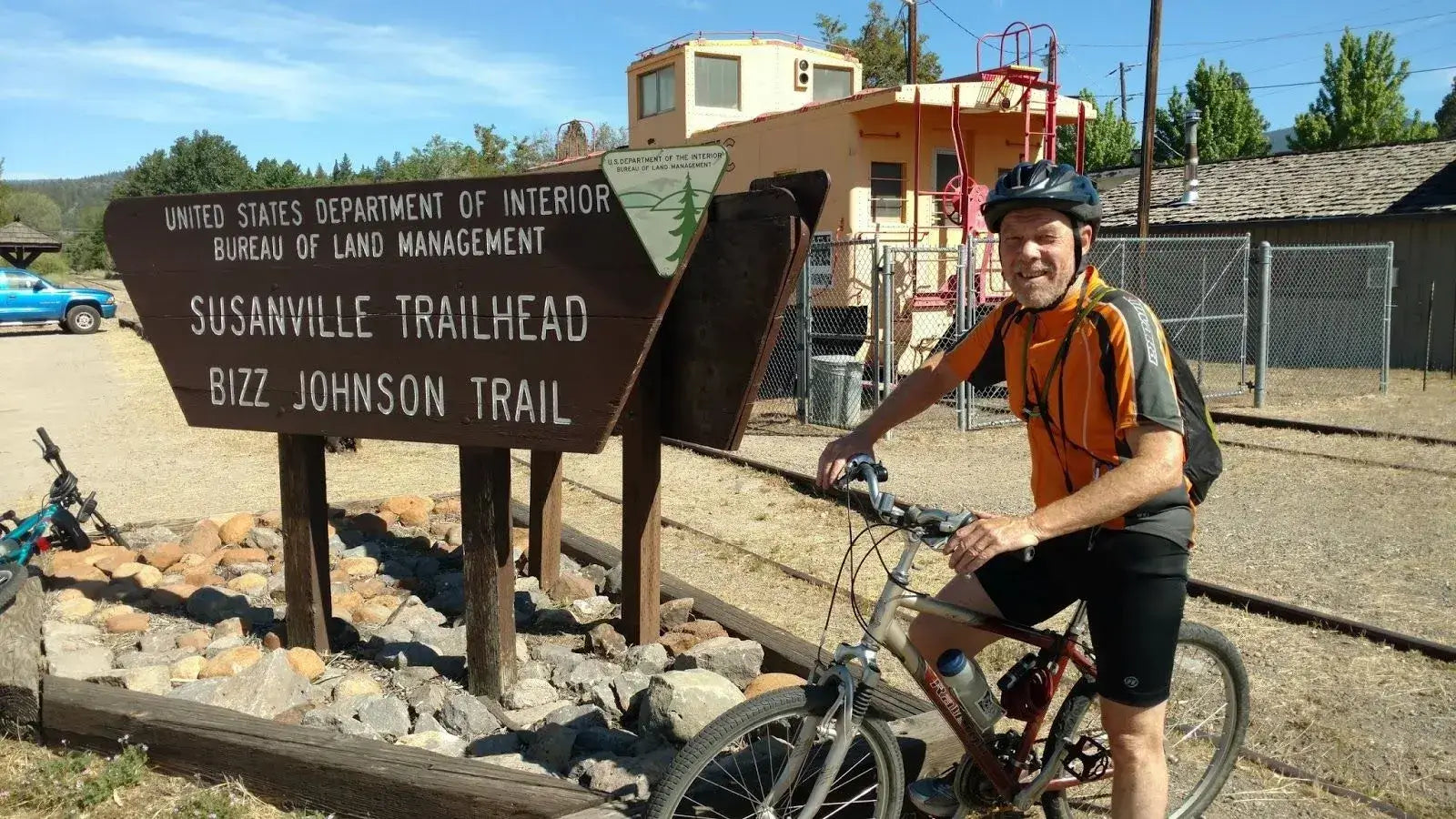 Cyclist posing with their bike at the Susanville Trailhead Bizz Johnson Trail sign on a sunny day.