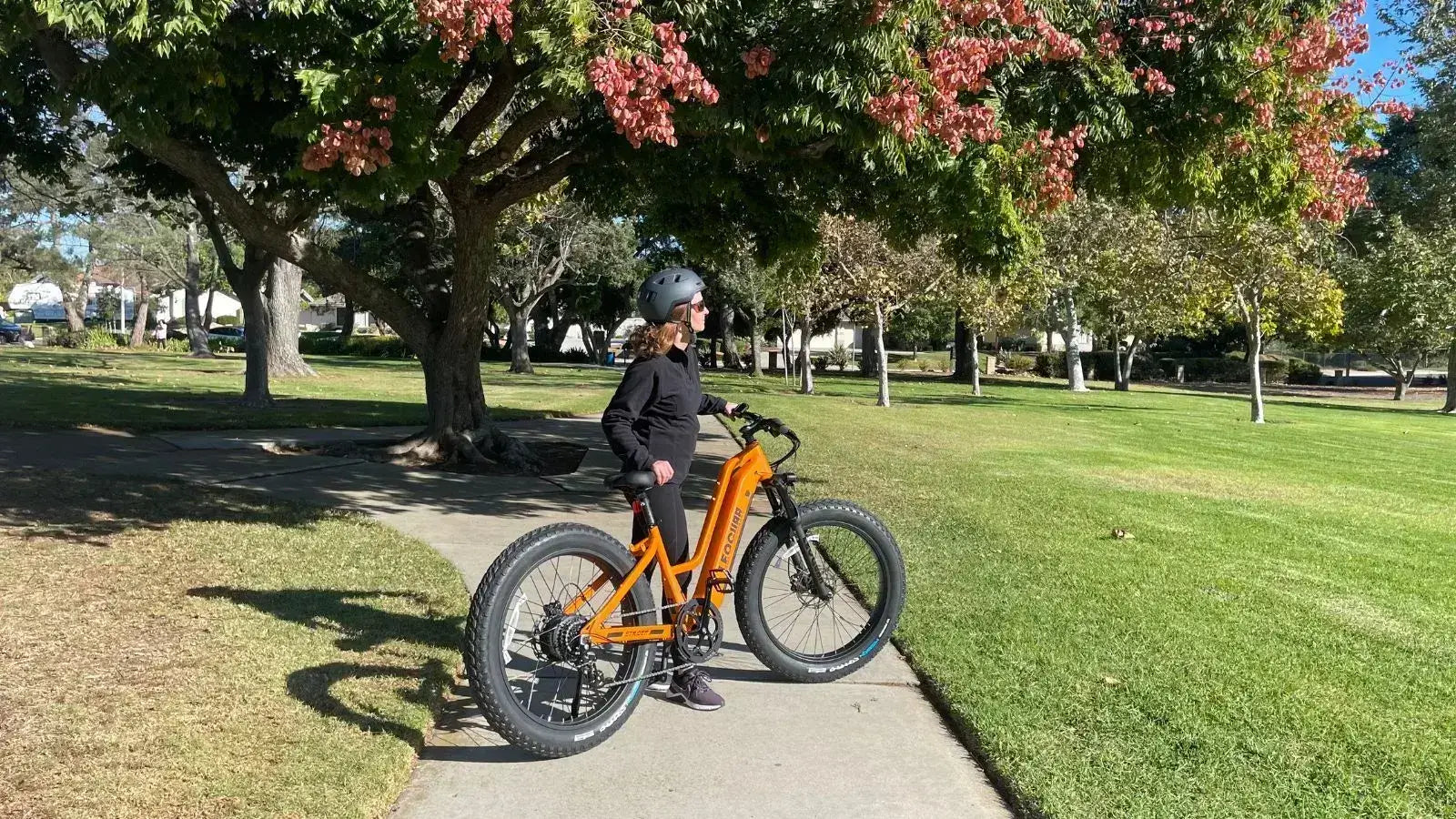 Rider on an orange 750W hub motor electric bike in a park, showcasing real-world usage and fall scenery