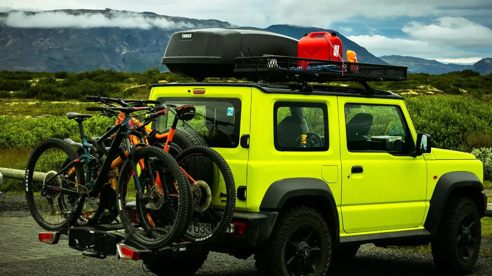 A bright yellow vehicle with a rooftop carrier and multiple bikes on an ebike hitch rack in a scenic outdoor setting.