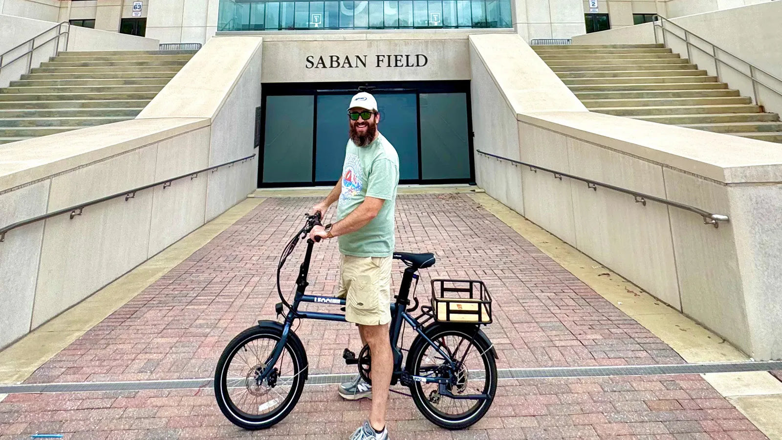 Man with a black folding electric bike in front of Saban Field buildin