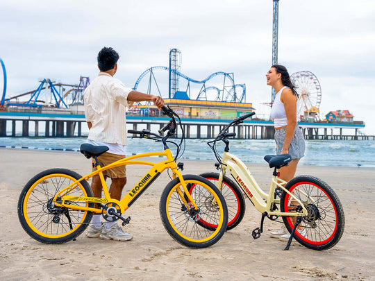 Man and woman riding Zephyr cruiser e-bikes near beach pier