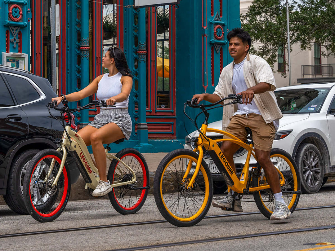 Man and woman riding Leoguar beach cruiser ebikes in city street with colorful architecture